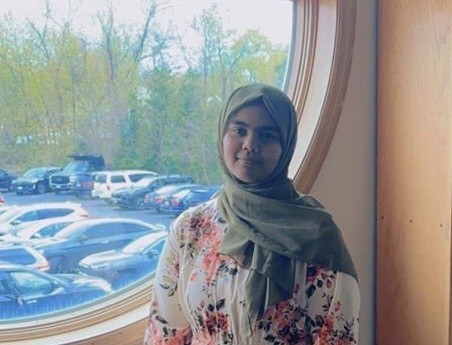woman with head scarf stands in front of circular window