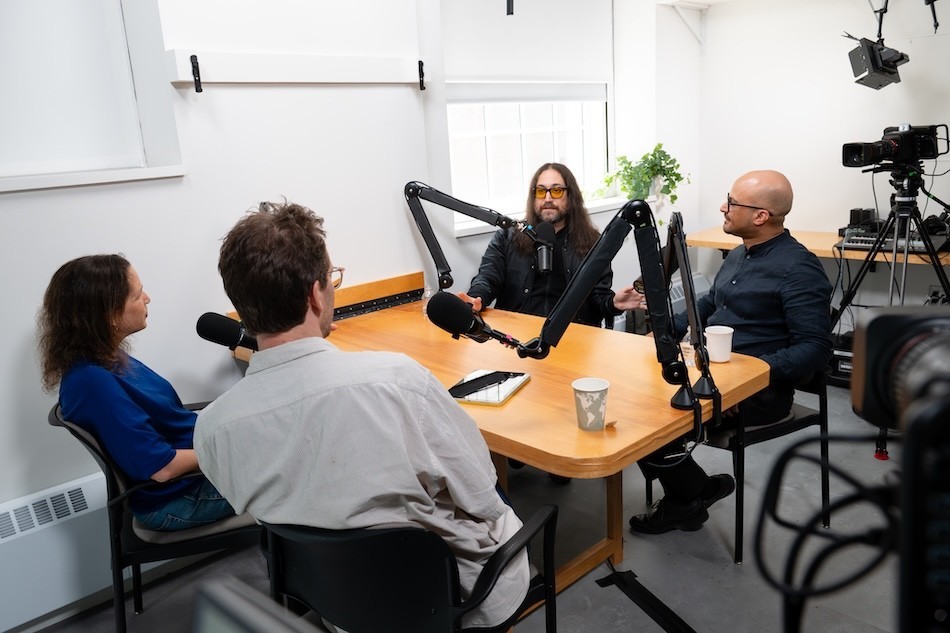 Four people sit around a table and talk into microphones