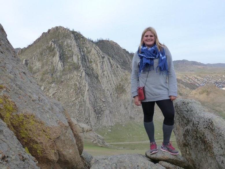 A Coverdell Fellow stands outside with the Mongolian mountains in the background.