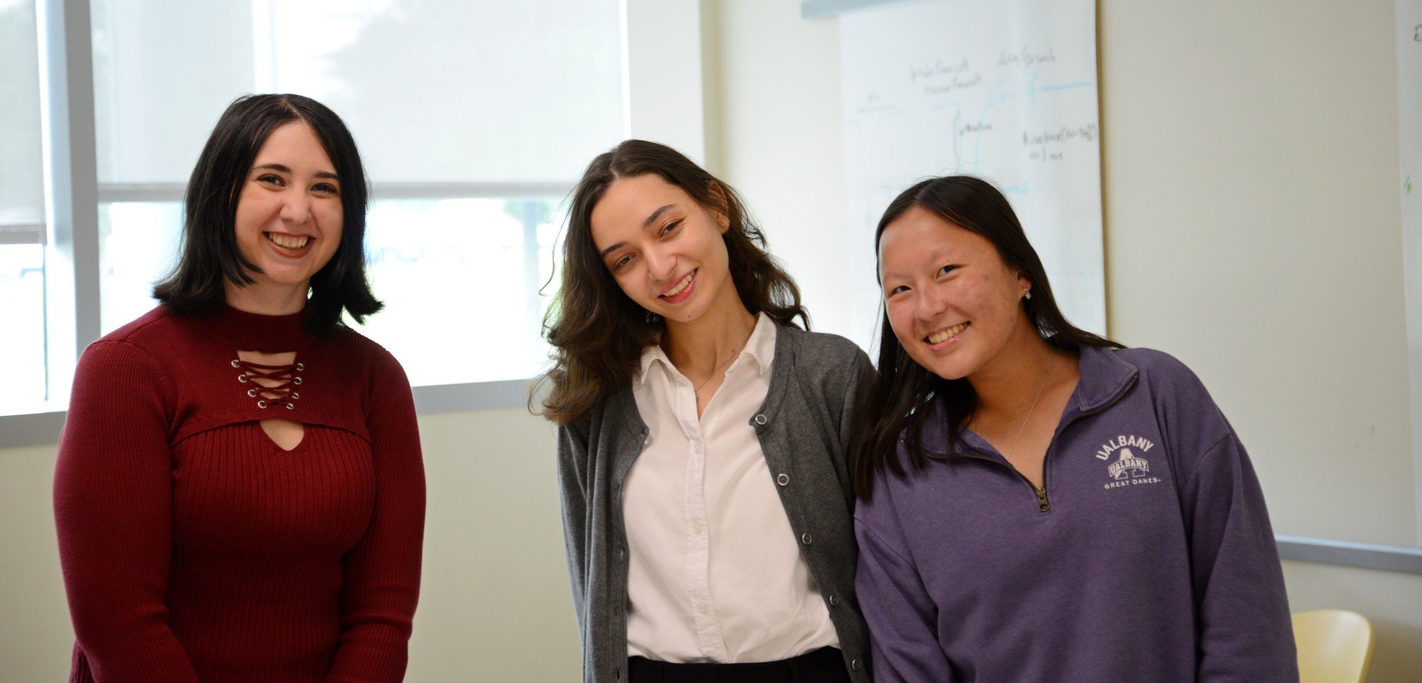 Three student researchers smile and pose for a photo inside the Niu Research Laboratory.