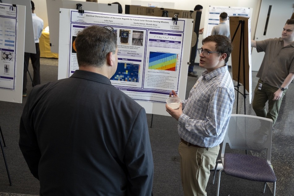 A young man talks to another man in front of a research poster