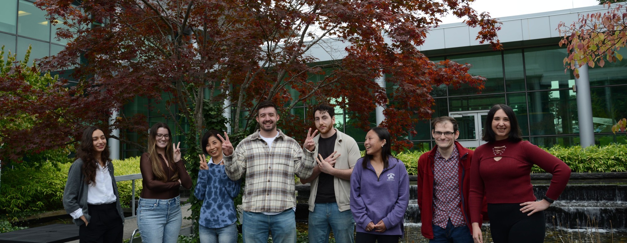 Research Scientist Megumi Akamatsu and seven student researchers laugh as they pose for a silly photo outdoors.