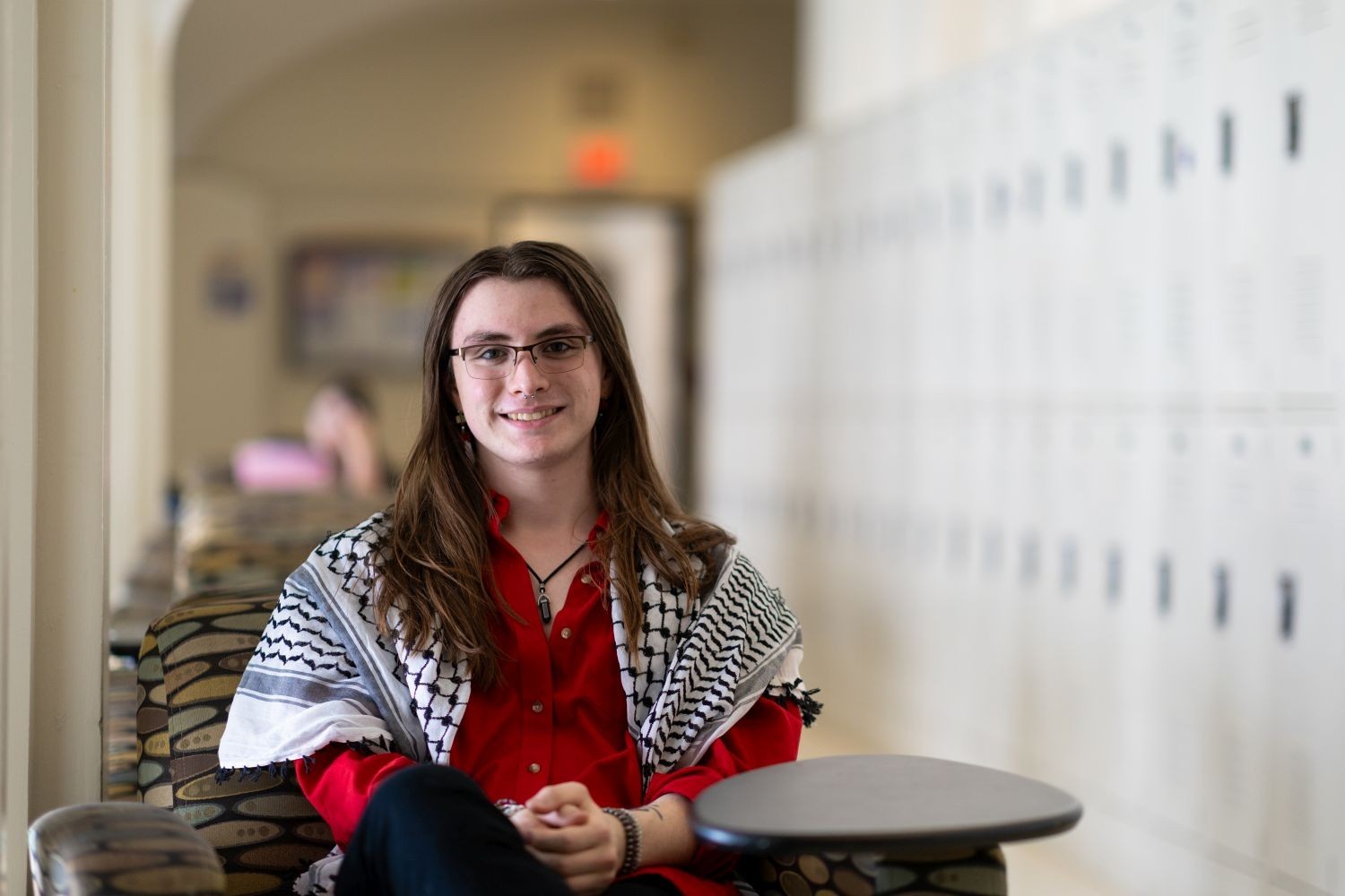 A person with long brown hair, wearing a red shirt and a black-and-white Keffiyeh 