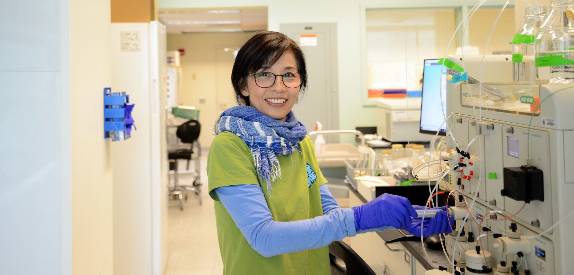 A Niu Research Laboratory team member smiles and poses for a photo while working on a piece of lab equipment.