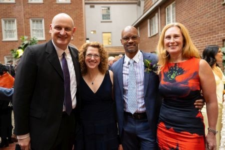 Two men and two women stand, arm in arm, smiling at the camera.