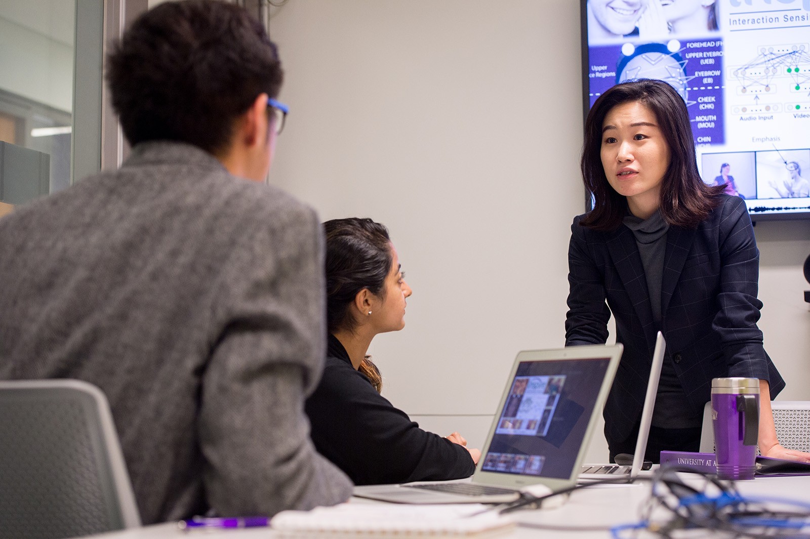 A faculty member speaks to two students with their laptops during a presentation