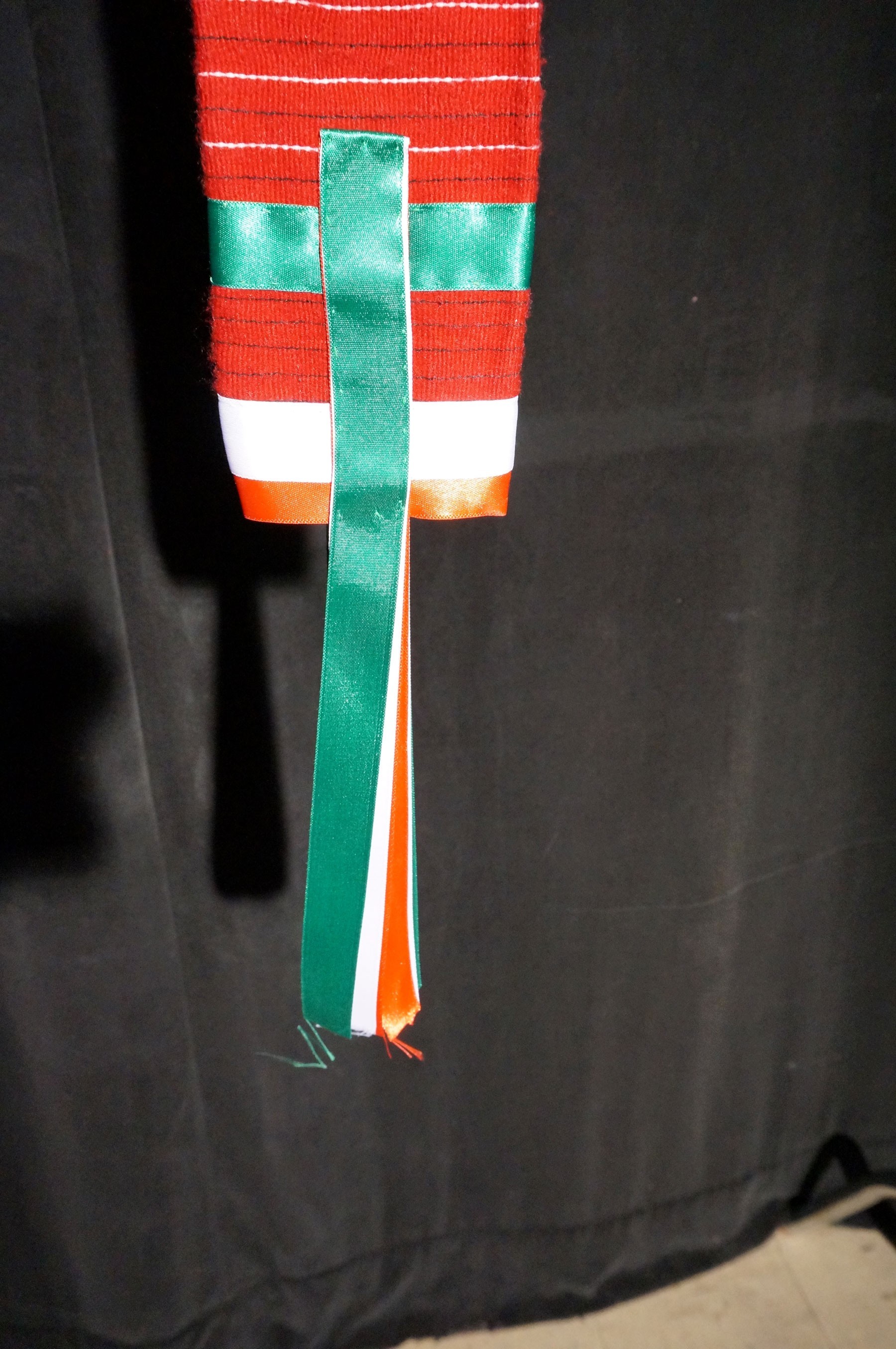 A man's red fabric belt with green, white and red silk ribbons.