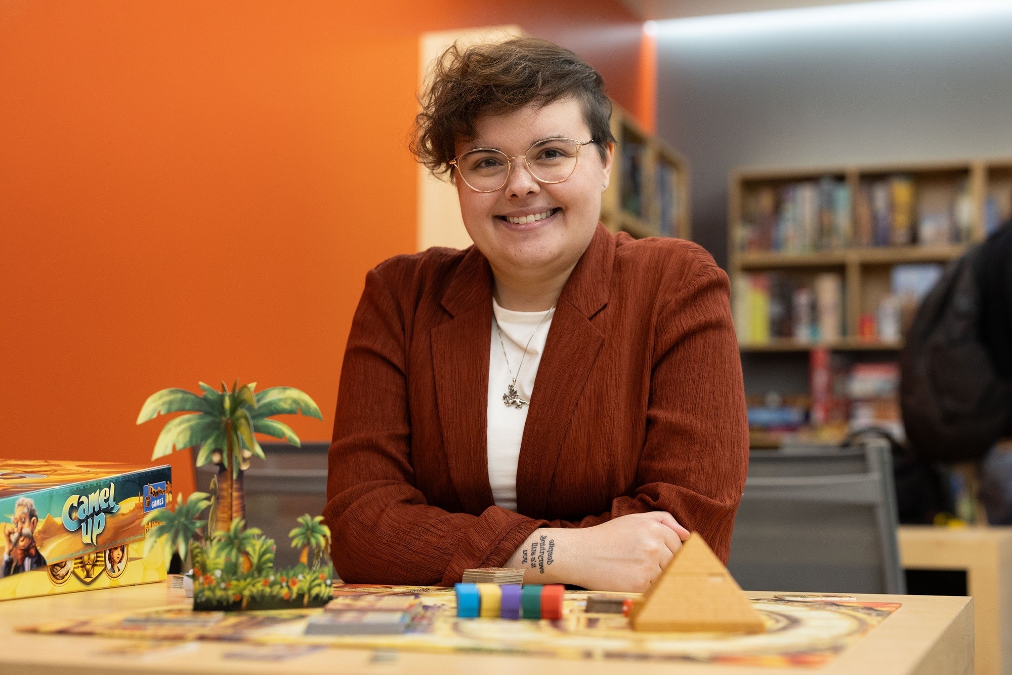 Claire Legato sits for a photo in front of a board game inside the Game Hub.