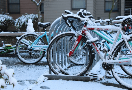 Several bicycles sit on a bicycle rack in the snow.