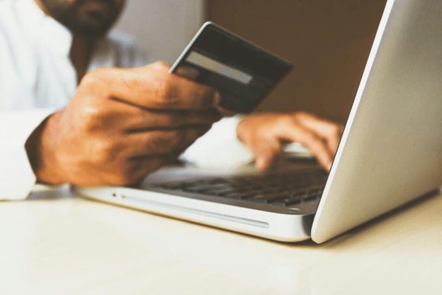 A person holds a credit card in their right hand while typing on a laptop with their left