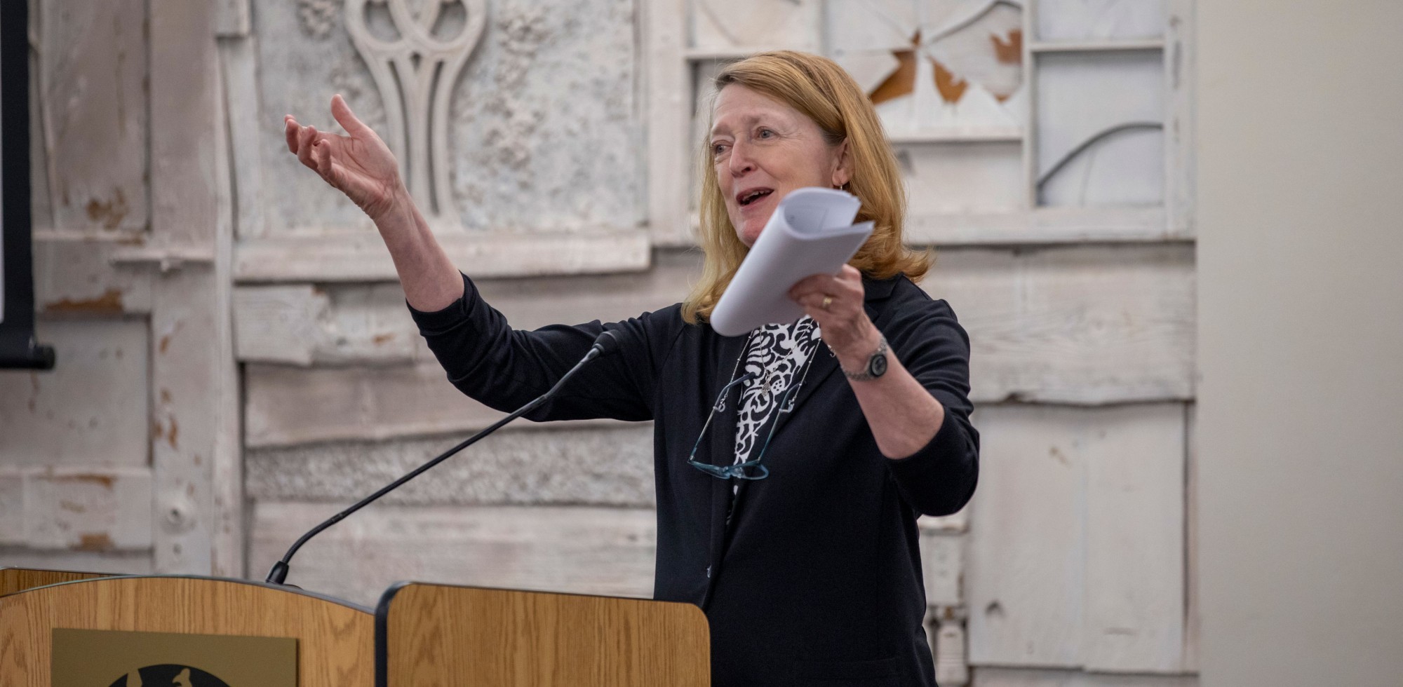 Dr. Annis Golden smiles and gestures with both hands while standing at a podium.