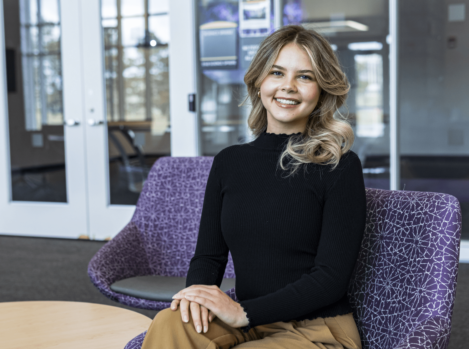 a smiling woman in a black sweater sits on a purple couch
