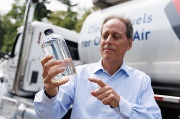 a man in a blue shirt holds a glass bottle with a clear liquid in it
