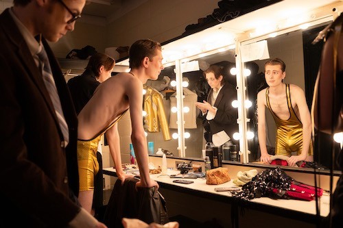 Student actors in costume and makeup look at themselves in the mirror backstage before dress rehearsals