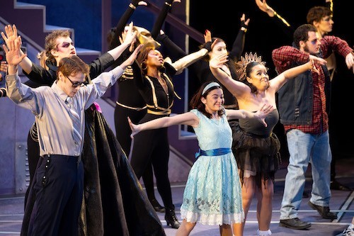 Student actors in costume and makeup dance on stage during dress rehearsals