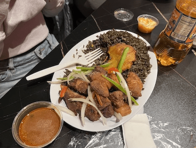 Fried pork, black rice and sliced veggies on a plate next to a bowl of sauce.