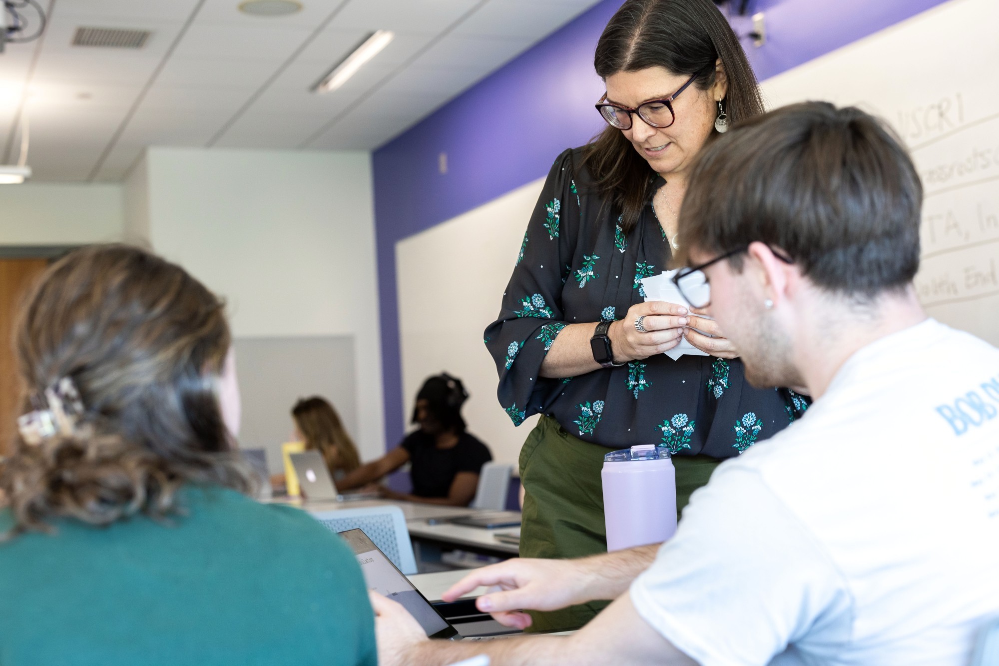 Professor Susan Appe talks with two students in the classroom. 
