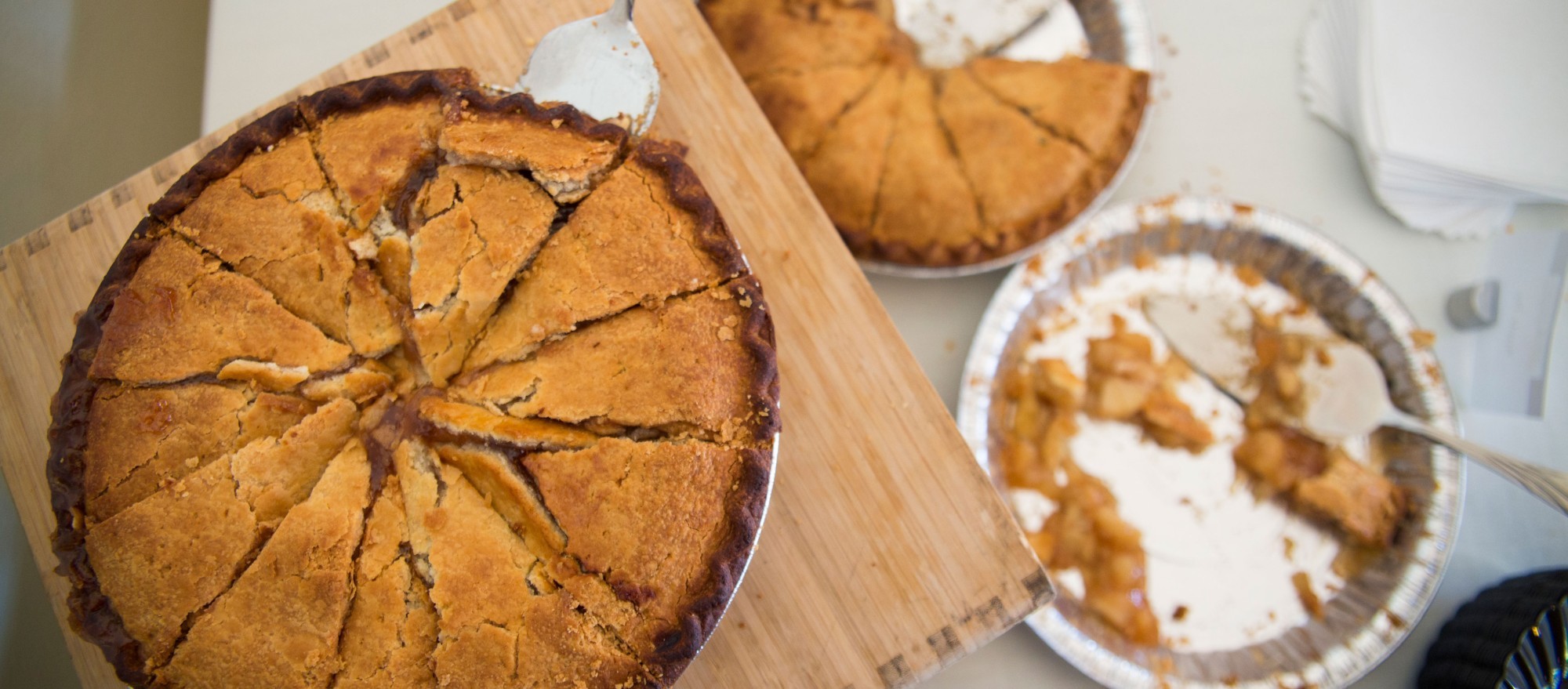 Three sliced pumpkin pies in aluminum tins. One pie is nearly eaten and another is partially eaten.