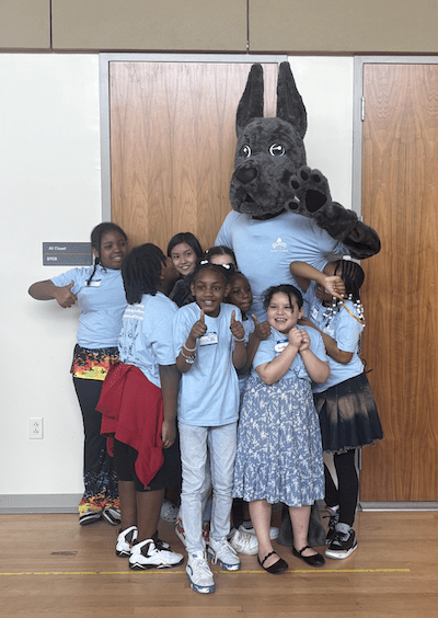 Children in light blue shirts excitedly pose with UAlbany mascot Damien