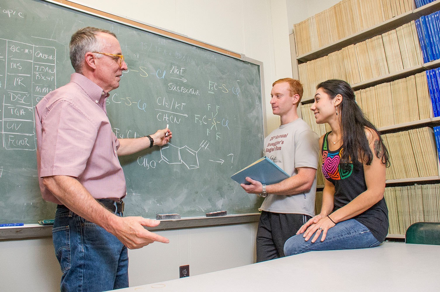 Two students working on formulas with a professor in a chemistry classroom.