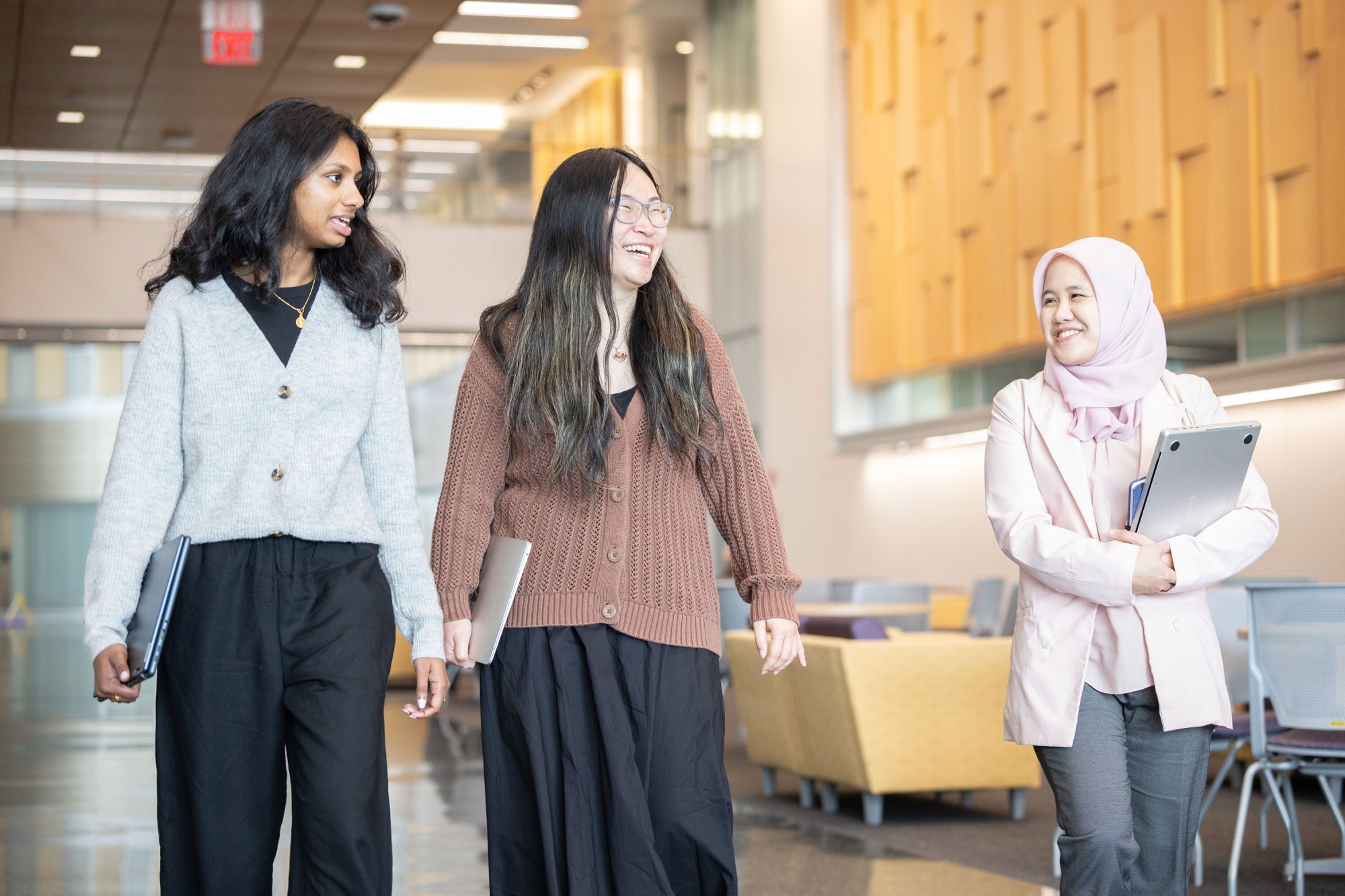 Three graduate students smile and laugh as they walk through UAlbany's ETEC building.
