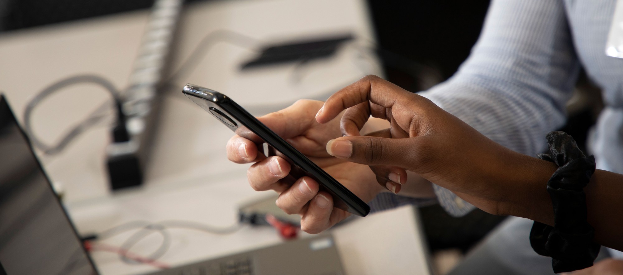 One person's hand holding a black cell phone and the other person's hand poised over the screen.