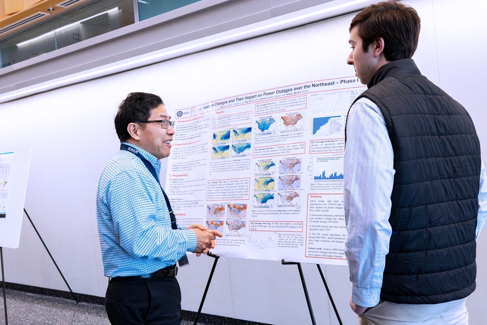 Two people have a discussion in front of a research poster presentation.
