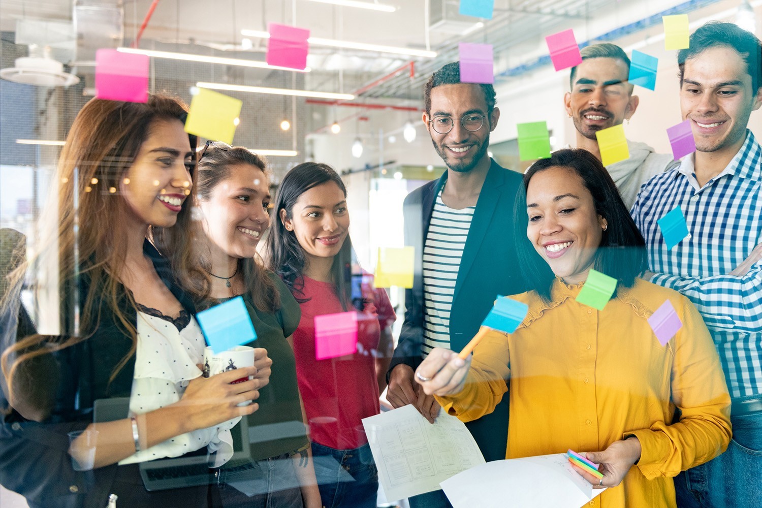 A group of young professionals planning tasks on glass wall with adhesive notes