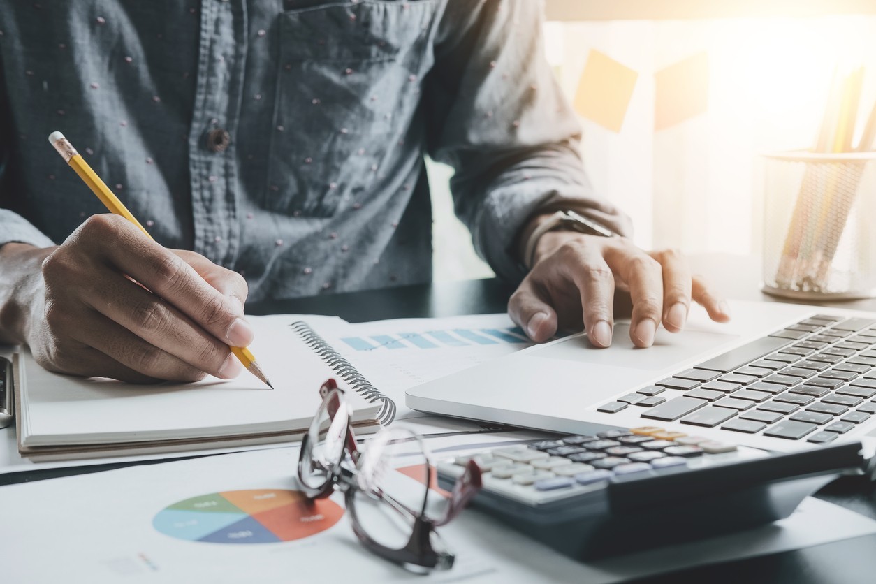 An accountant making notes and working on a laptop