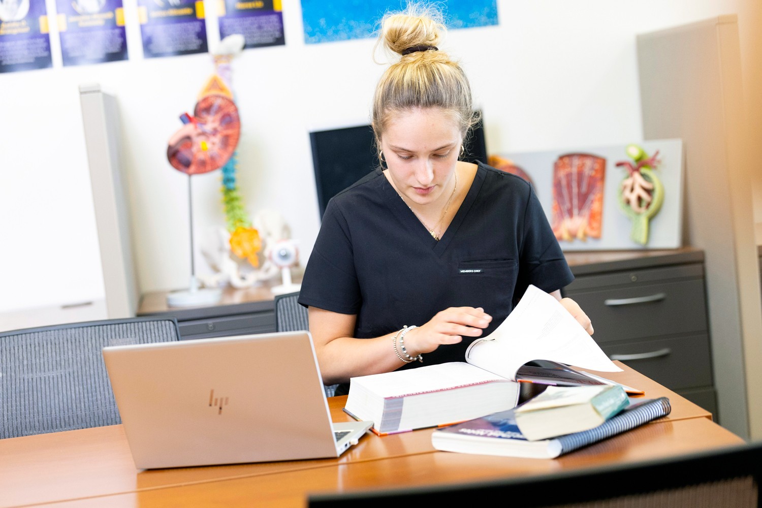 A nursing student studying with textbooks and a laptop.