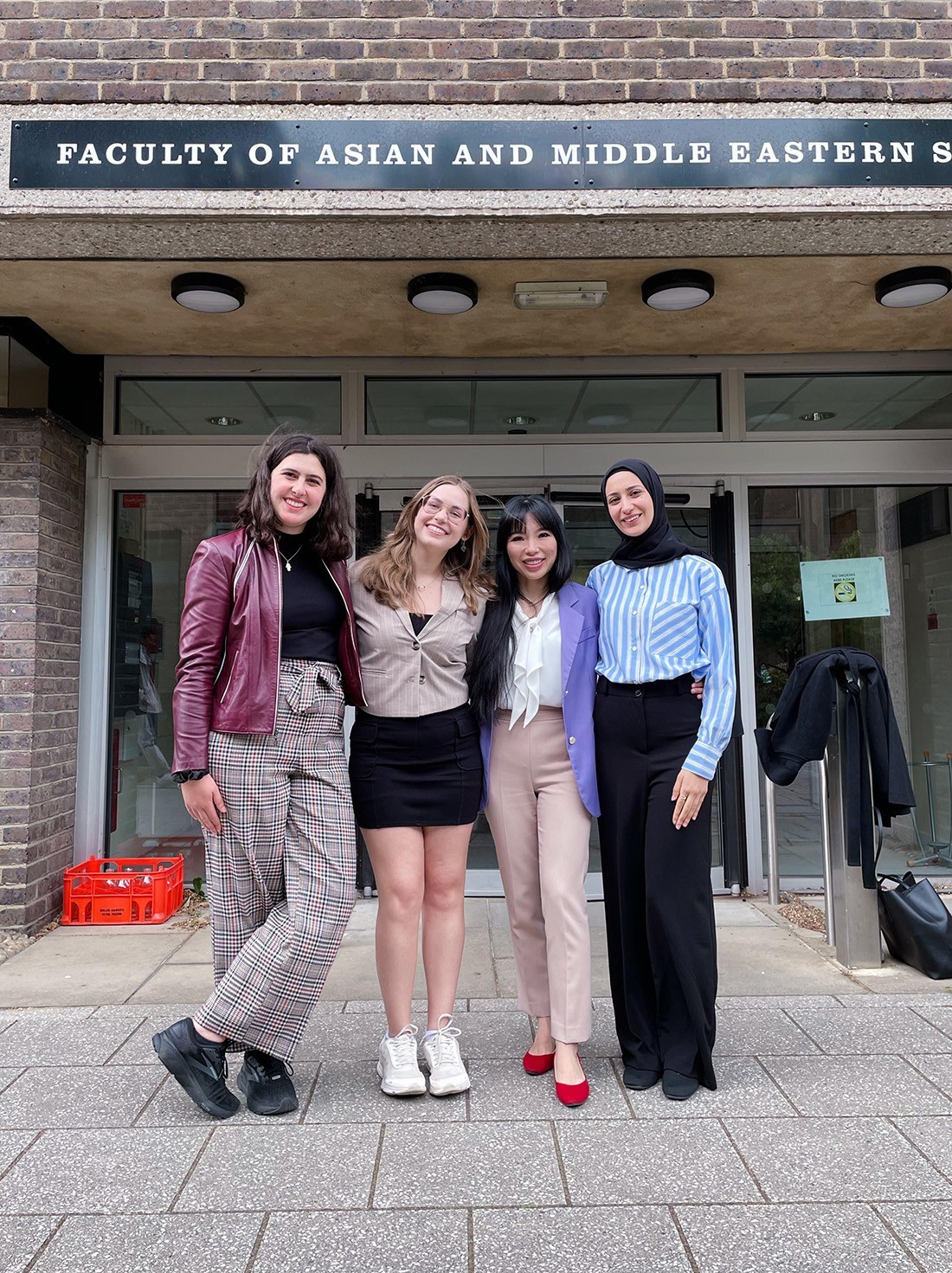 Four female students stand in front of a Facutly of Asian and Middle Eastern Studies sign at Cambridge