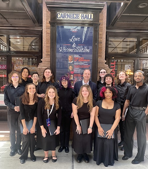 A group of students dressed in black stand in rows for a portrait in front of famed Carnegie Hall in NEw York city.