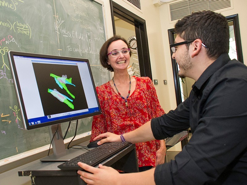 Biology students discussing research in front of a computer monitor.