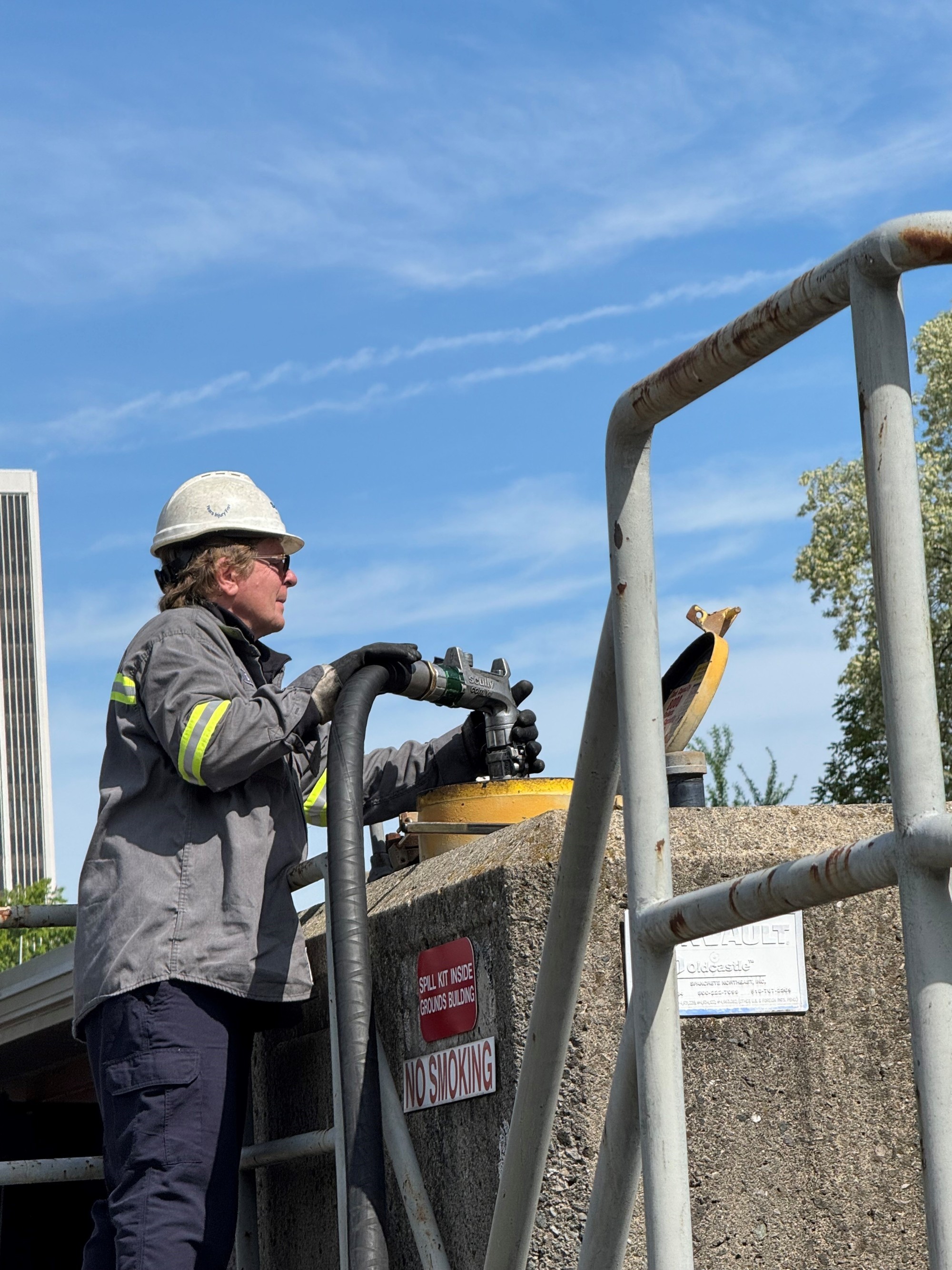 a man in a grey jacket and a white hardhat puts fuel into a tank
