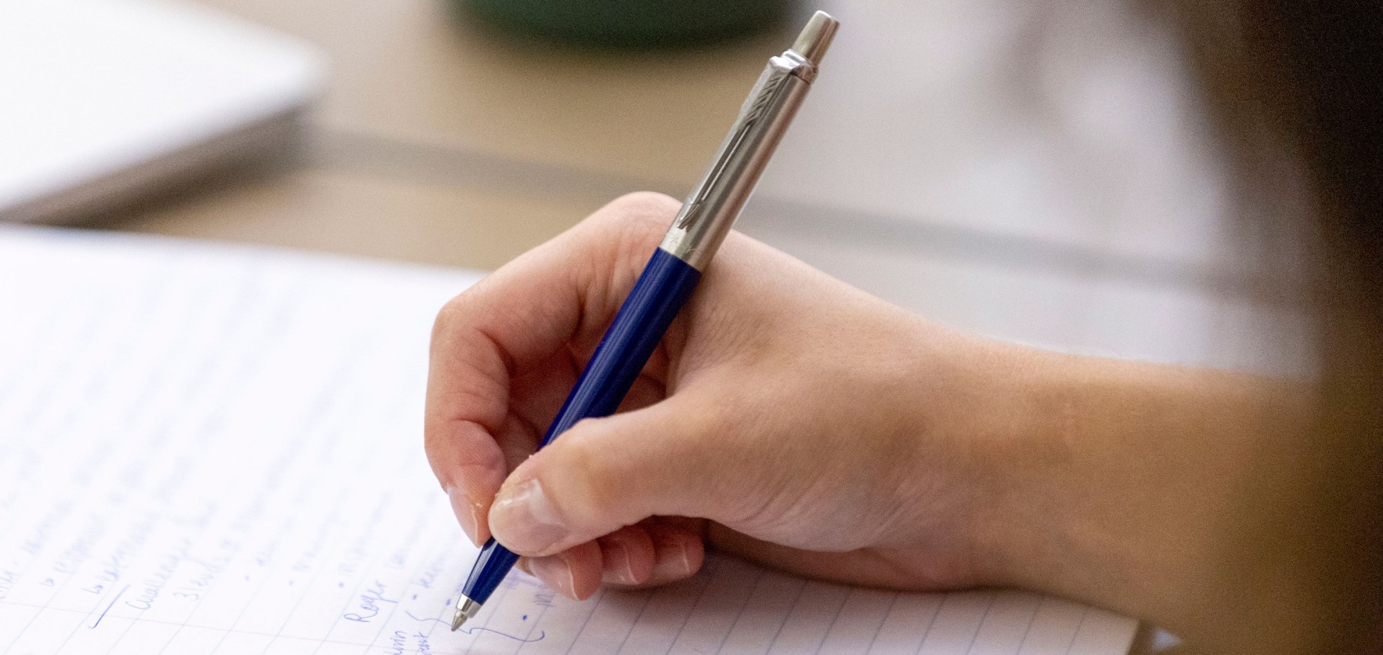 A student writes in a notebook using a blue pen.