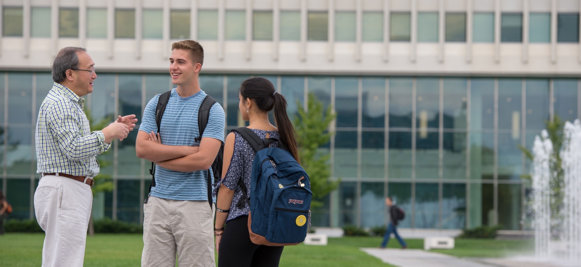 A faculty member smiles and gestures as he speaks with two students outside.