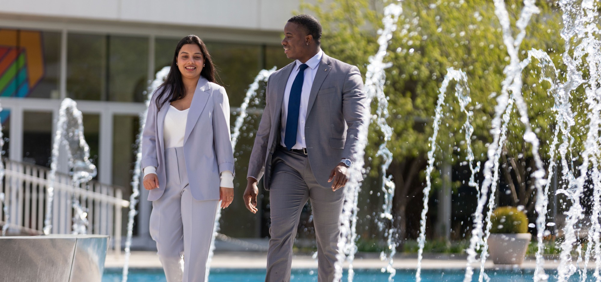 Two UAlbany graduate students wearing suits walk around the main fountain on the Uptown Campus.