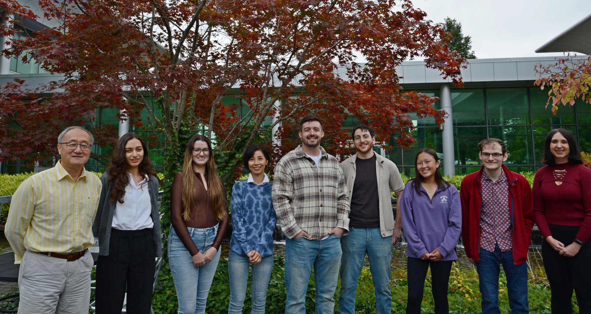 Dr. Li Niu, Research Scientist Megumi Akamatsu and seven student researchers smile and pose for a photo outdoors.