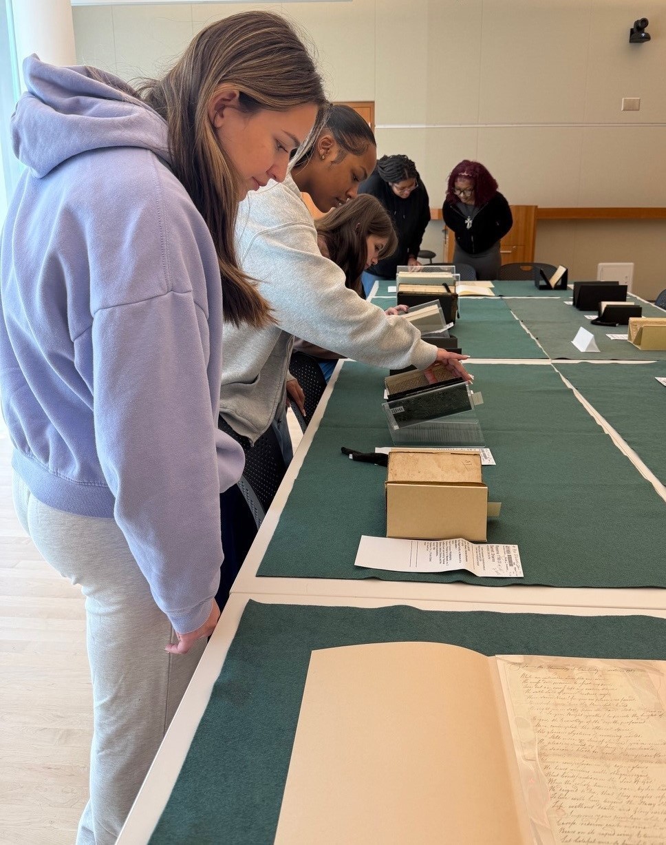 Five students standing and looking at antiquarian objects.