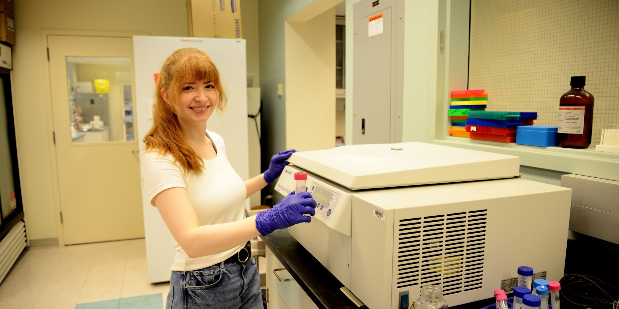 A student researcher smiles and poses for a photo with a piece of equipment inside the Niu Research Laboratory.