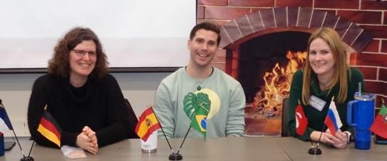 Three people are seated at a table topped with flags from around the world.