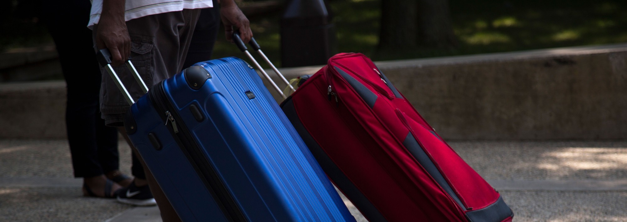 A student wheels two suitcases down a pathway.