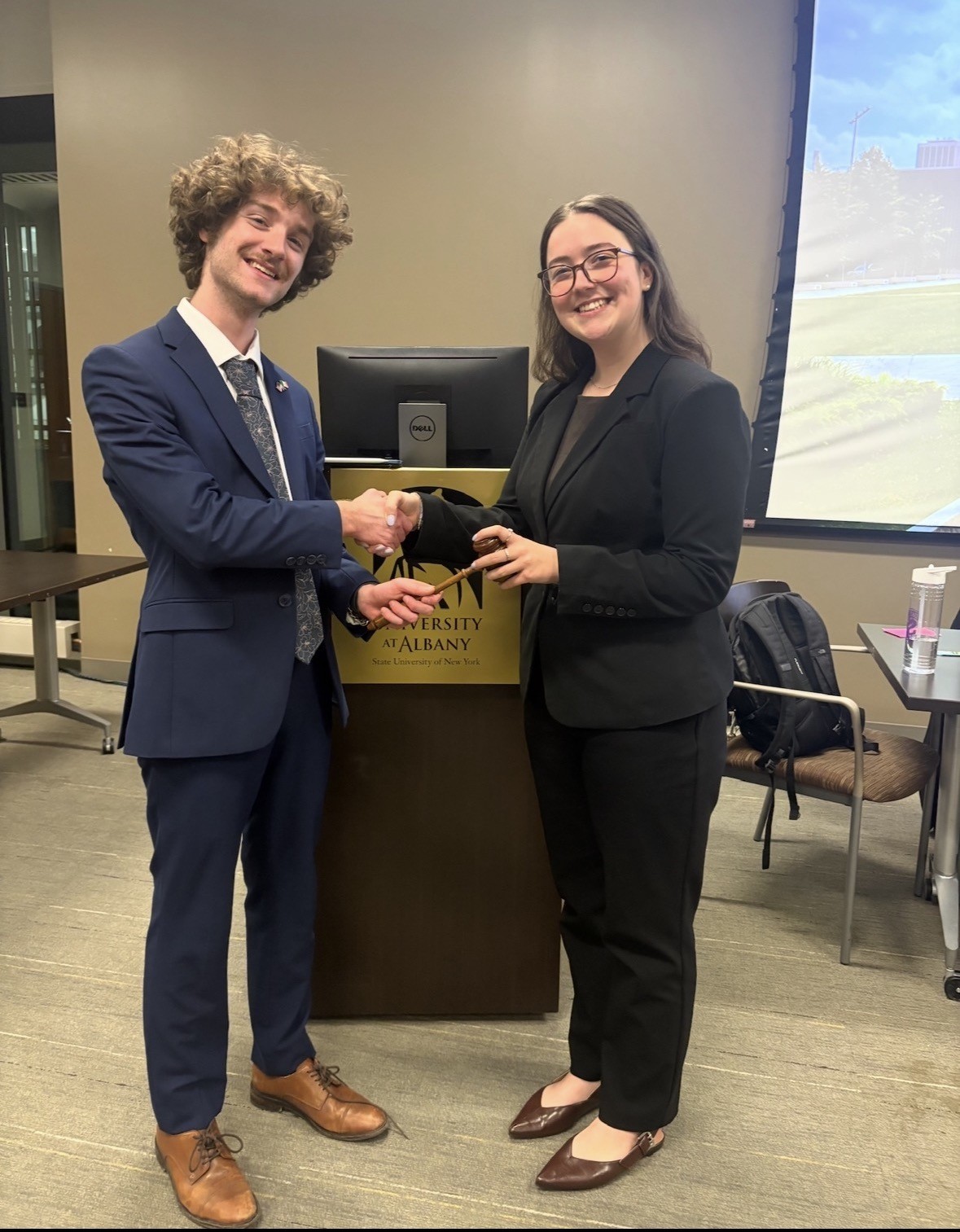 Junior Troy Serao shakes hands with a fellow classmate in front of a UAlbany podium.