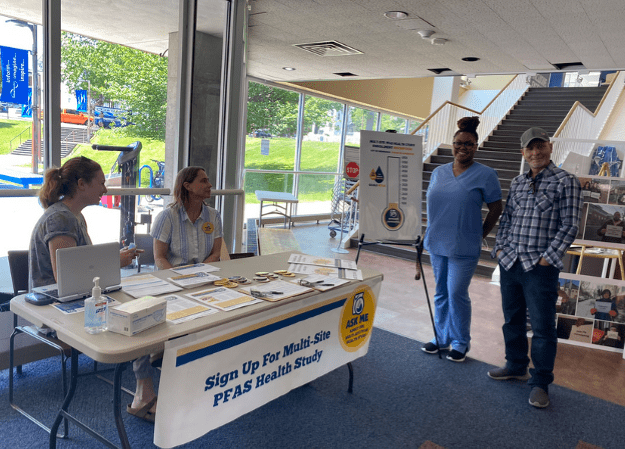 Two people sitting at an information table and then there are two people standing next to it.