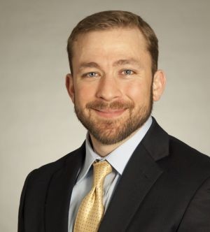Headshot of Justin Picket, in a dark jacket and yellow tie