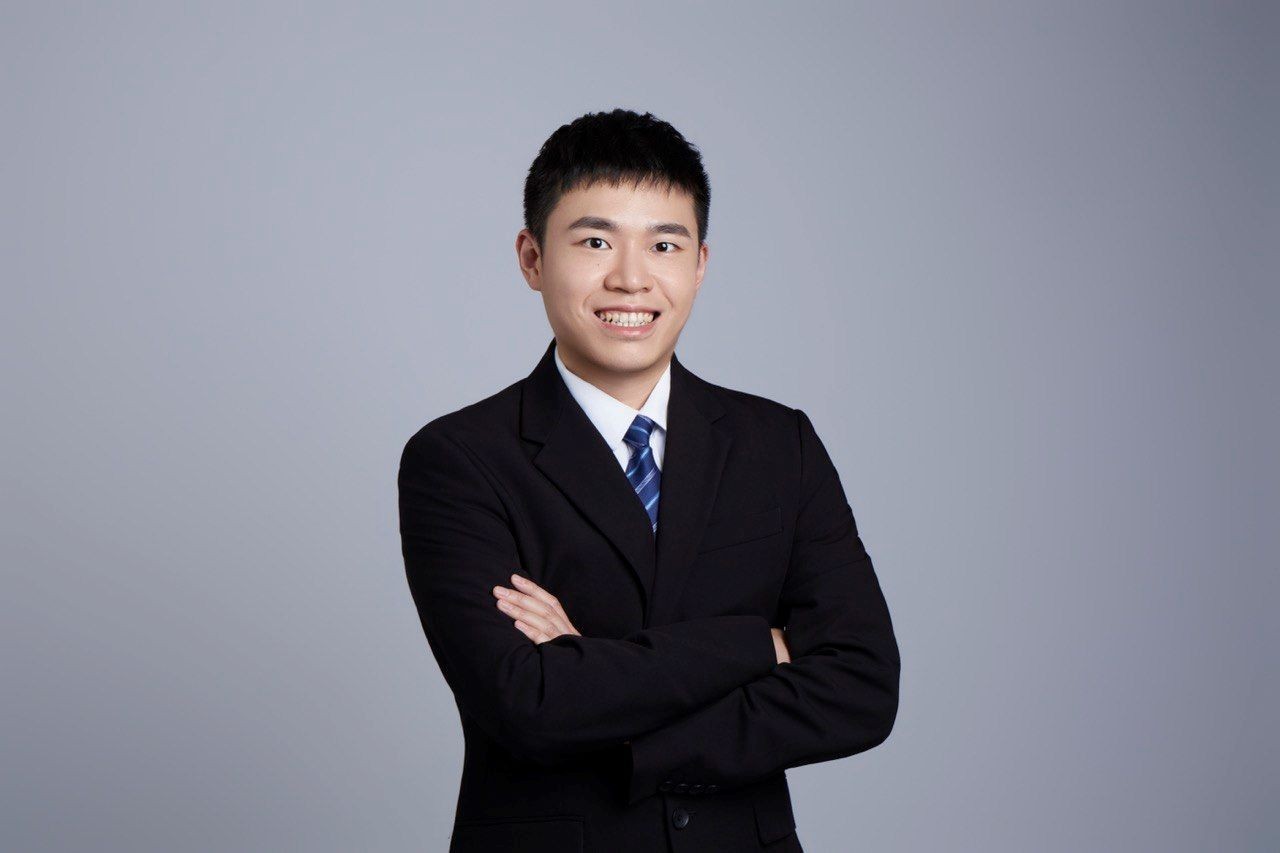 A profile photo of Zong-Xian (Sam) Huang wearing a dark suit and tie against a gray background
