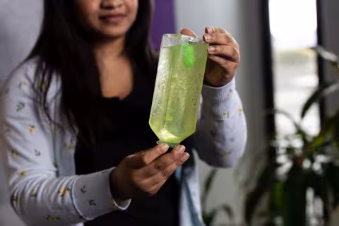 A woman holds a clear plastic water bottle filled with green liquid an glitter upside-down to produce a sparkling snowglobe effect.  
