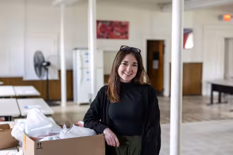 A woman poses for a portrait with her arm propped on a cardboard box filled with full plastic bags. 