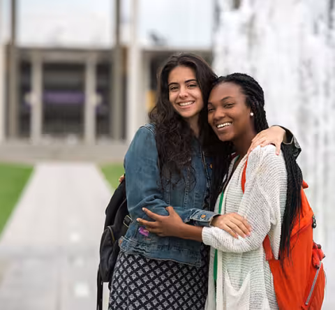 Two students stand, smiling in front of the Campus Center Fountains.