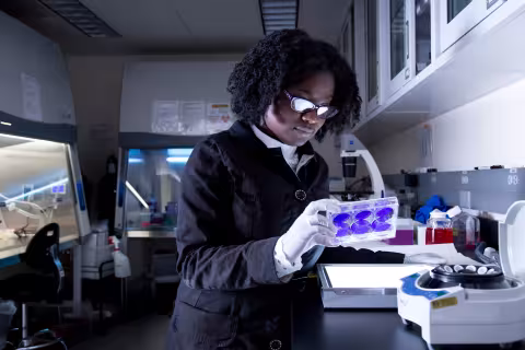 A Biological Sciences student sits inside a lab and looks at a sample dish.